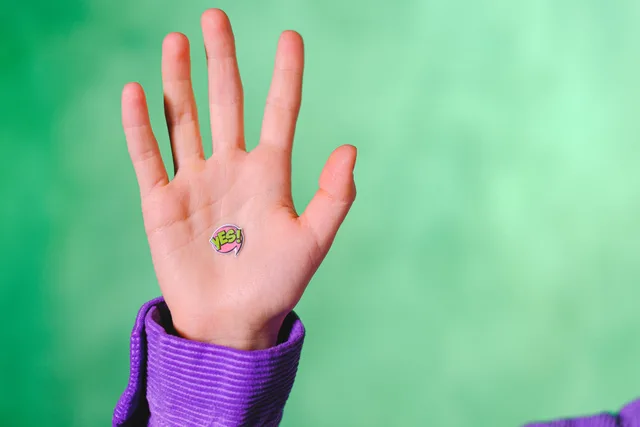 Crop anonymous person demonstrating sticker with word Yes placed on hand against green background. AdTech privacy and permission signals